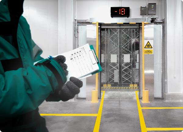 Een werknemer die handschoenen en een jas draagt, vinkt items op een lijst af in een diepvriesmagazijn. Het magazijn is netjes opgedeeld in verschillende zones met behulp van ToughStripe Cold-vloertape.