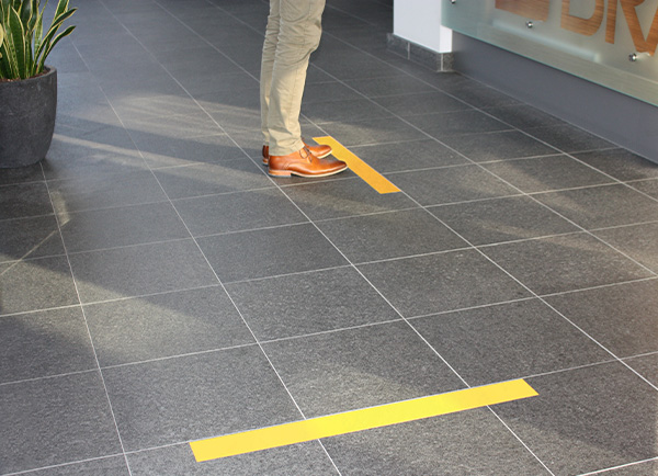 Een persoon gebruikt zijn handen om ToughStripe Vinyl-vloertape te verwijderen van vinyltegels. De tape laat zich in één stuk verwijderen.