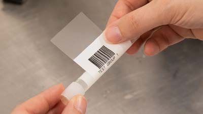 Een zelflaminerend polyesterlabel van Brady met een barcode erop geprint wordt rond een testbuisje gewikkeld.